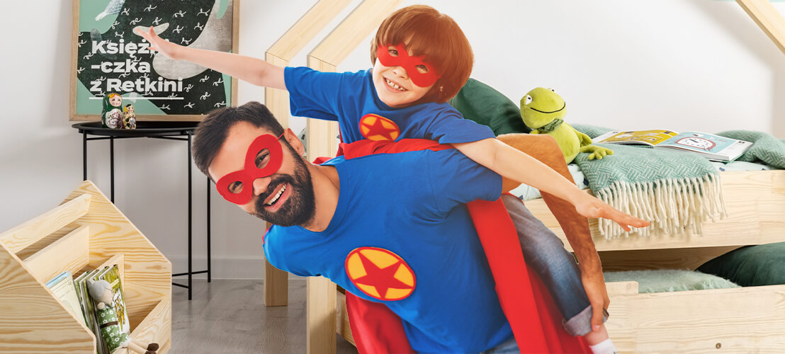 Un enfant souriant, juché sur le dos de son père, vêtu d'un costume de super-héros, semble très heureux et fier de son nouveau lit cabane