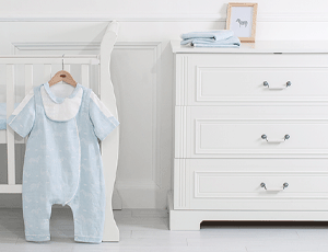 Commode blanche dans une chambre de bébé avec un pyjama bleu suspendu à côté