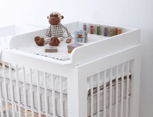 Plan à langer posé sur un lit bébé avec une peluche singe et des jouets - Meuble de chambre bébé